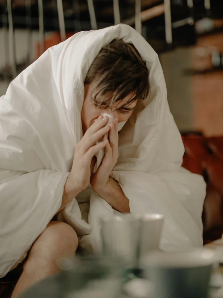 Person wrapped in a blanket sneezing into a tissue, showing cold or flu symptoms