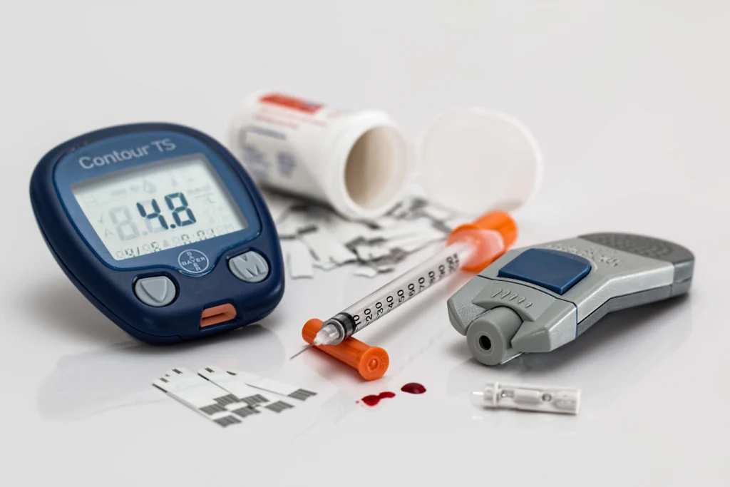 Glucometer showing blood sugar reading with insulin syringe, lancet device, and test strips for diabetes management