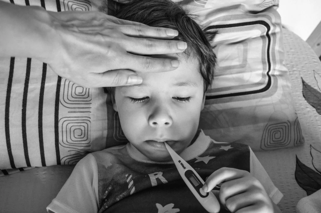 Fever temperature check in a child using a digital thermometer while a parent monitors symptoms at home