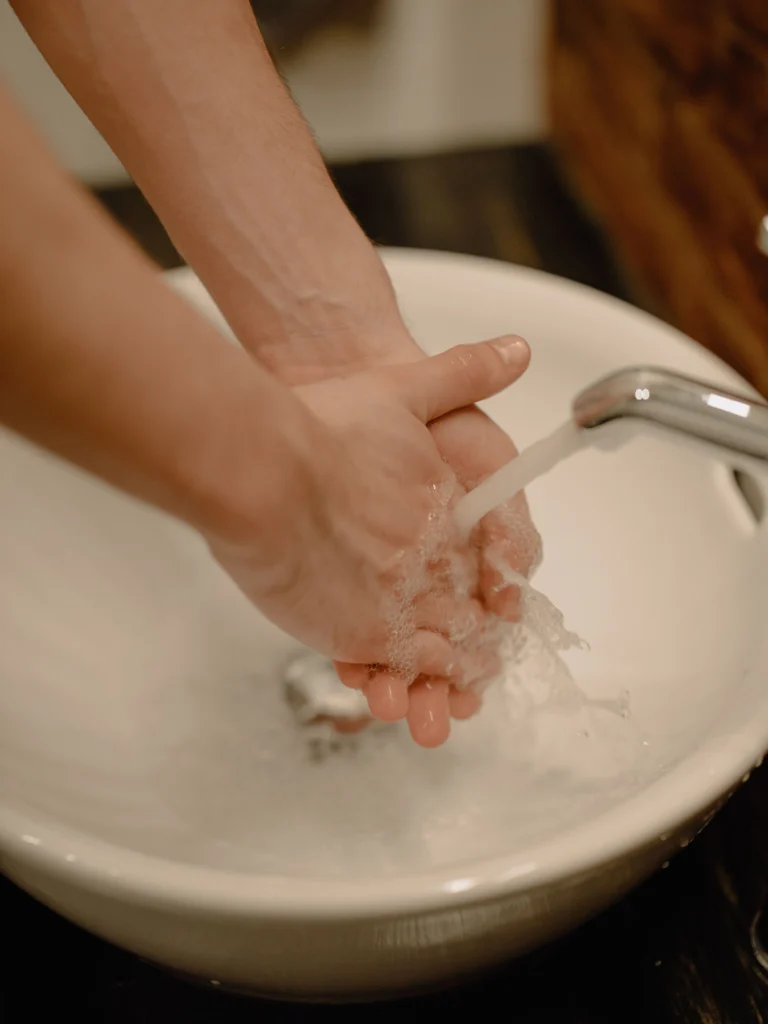 Person washing hands under running water, a common cause of dry skin (xerosis) due to loss of the skin's natural moisture.