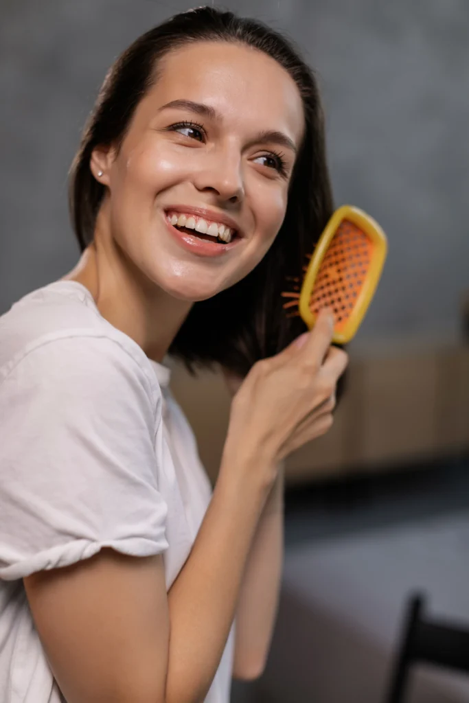 Woman gently brushing her hair as part of a healthy hair care routine to reduce breakage and keep hair smooth
