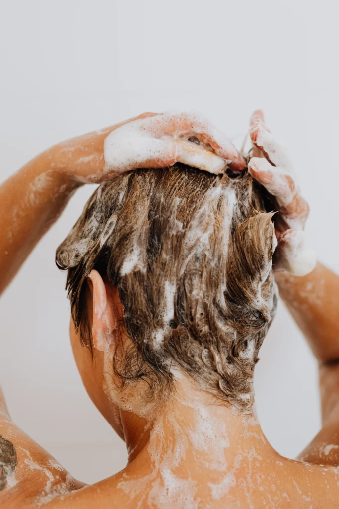 Person washing their hair with shampoo as part of a healthy hair care routine to maintain a clean and healthy scalp